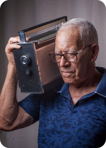 An older man wearing glasses holds a vintage radio near his ear, eyes closed in calm reflection
